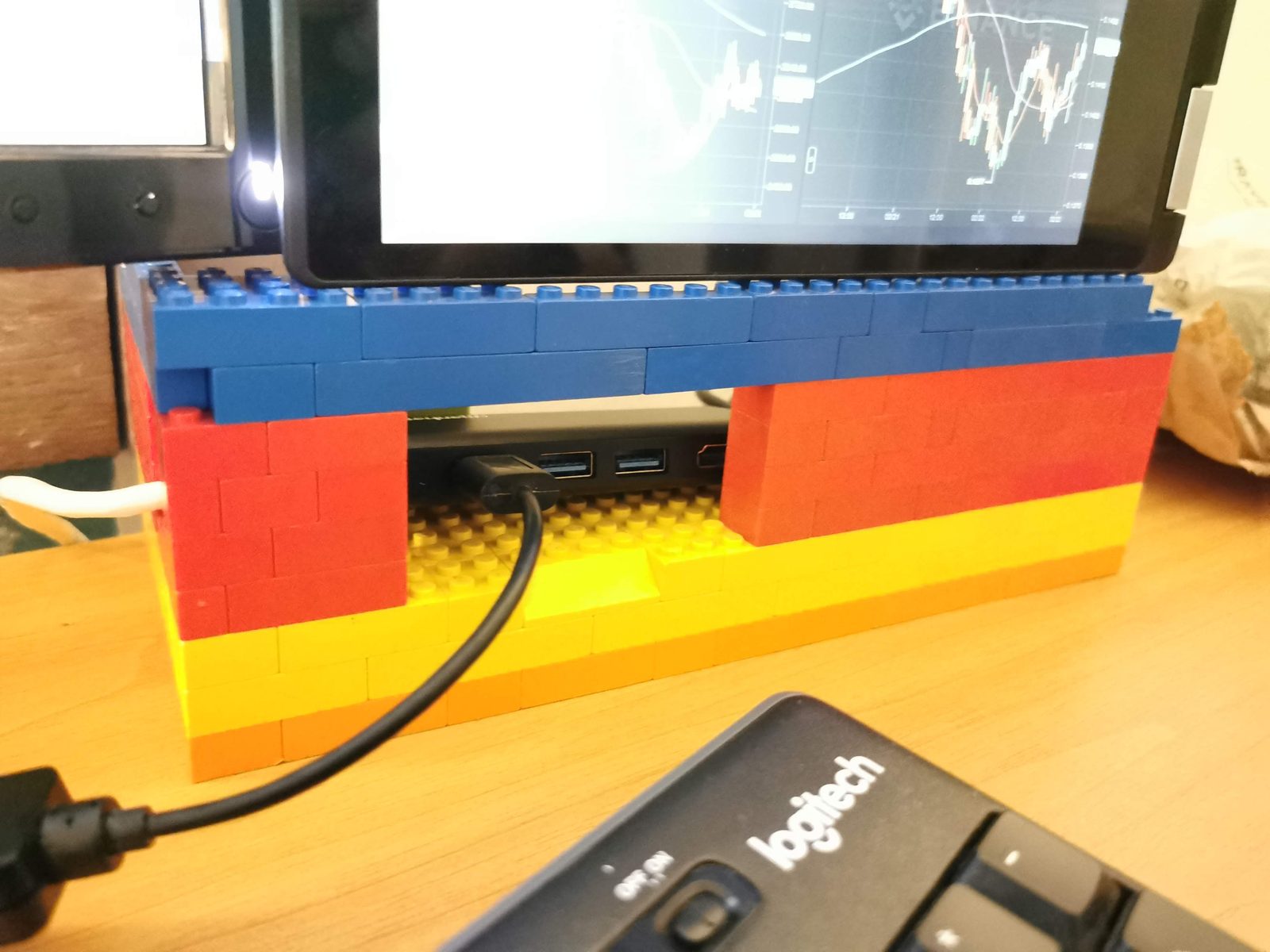 Crveni i plavi LEGO blokovi poredani u tornjeve na radnom stolu pred monitorom s grafikonima.