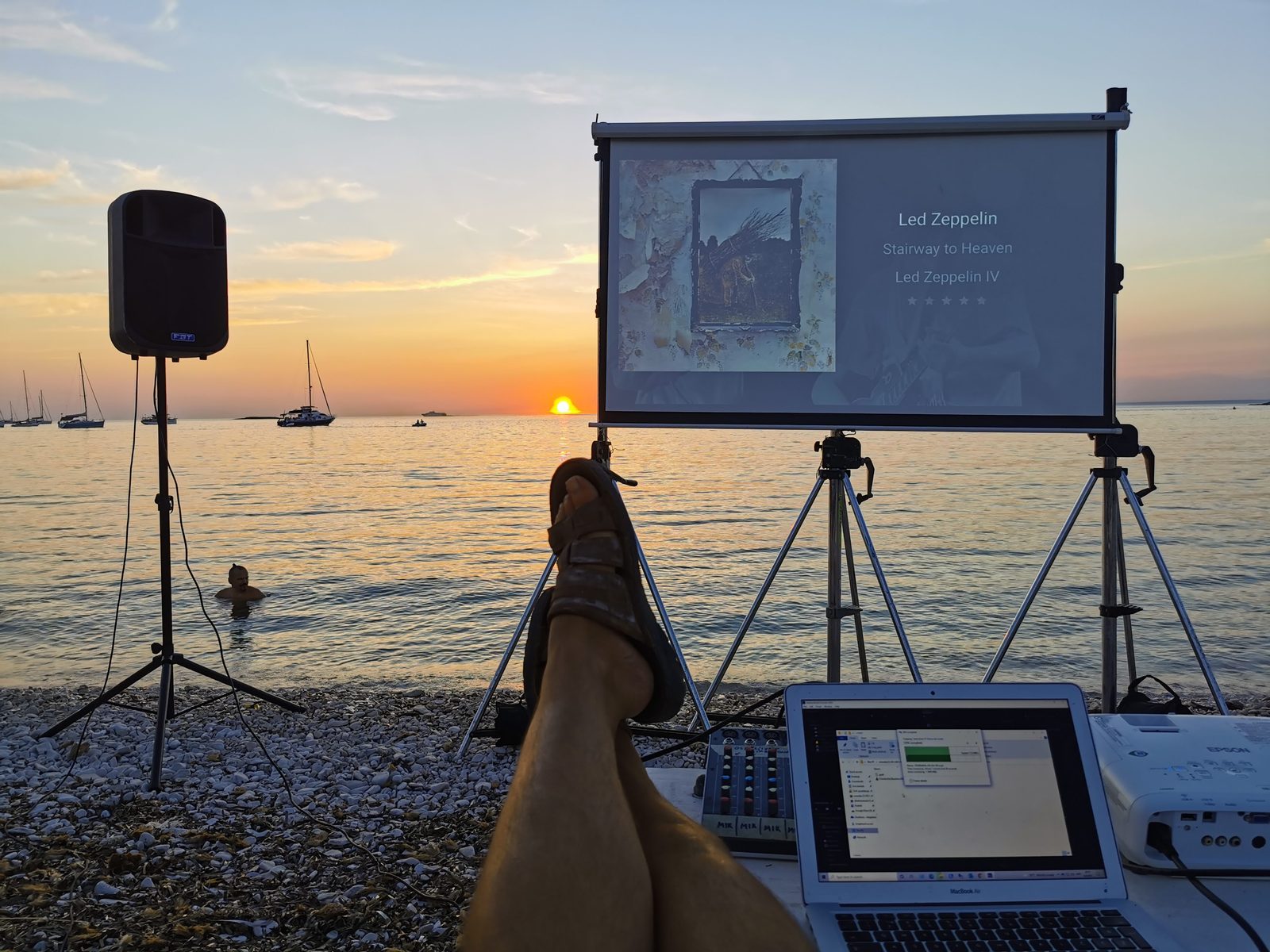 Laptop i prijenosni projektor postavljeni na obali pri zalasku sunca.